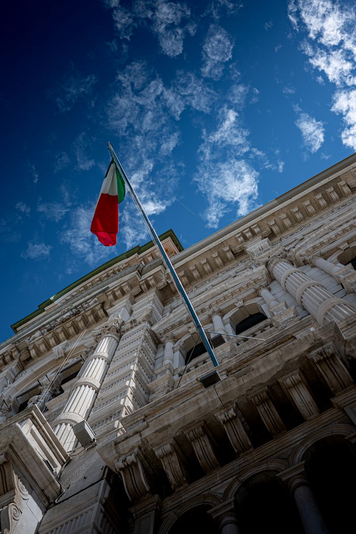 Il palazzo del Municipio di Trieste visto dal basso, con il tricolore sull’asta e le nuvole nel cielo blu.