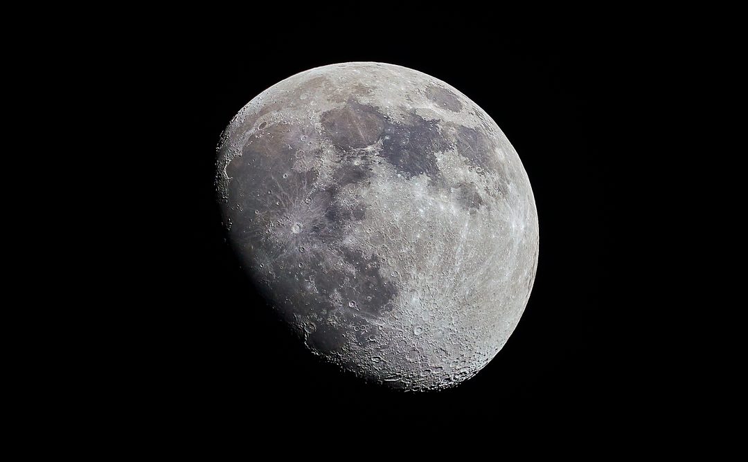La luna quasi piena con i crateri nitidi sul cielo nero.