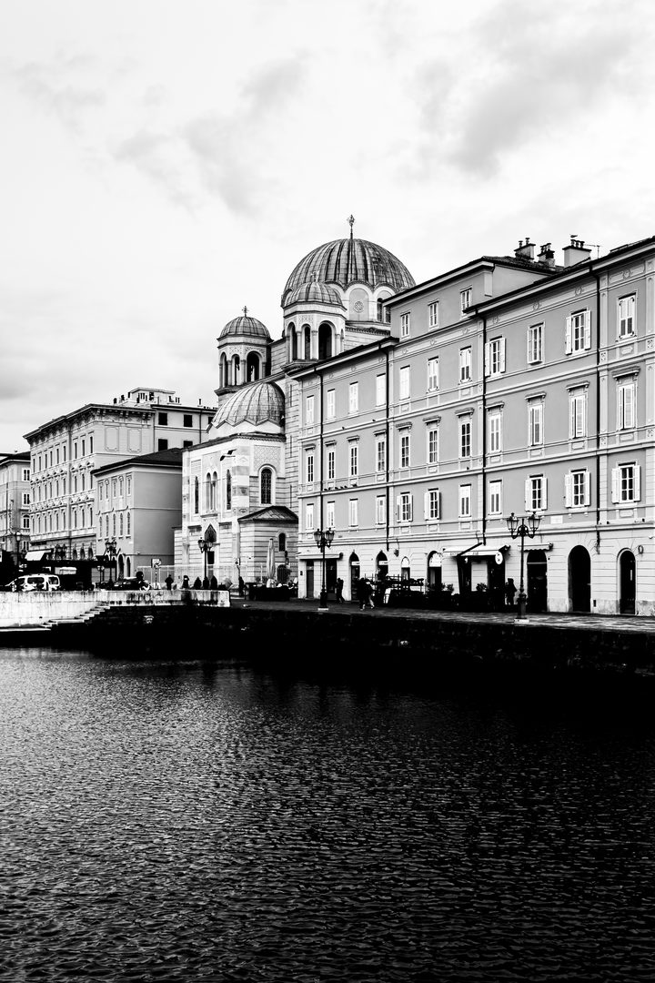 Bianco e nero: il Canal Grande di Trieste con la chiesa di San Spiridione, i palazzi e l’acqua increspata in primo piano.